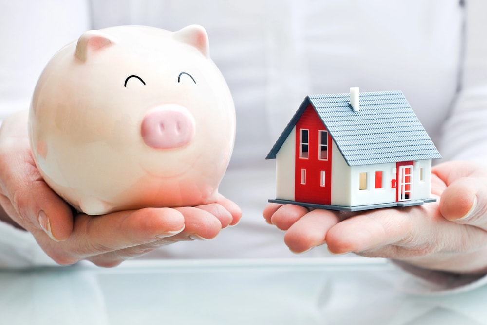 a person holding a piggy bank and a model house in either hand to demonstrate property taxes