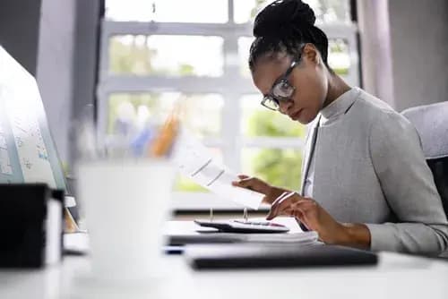 Woman typing on a calculator and holding a sheet of paper